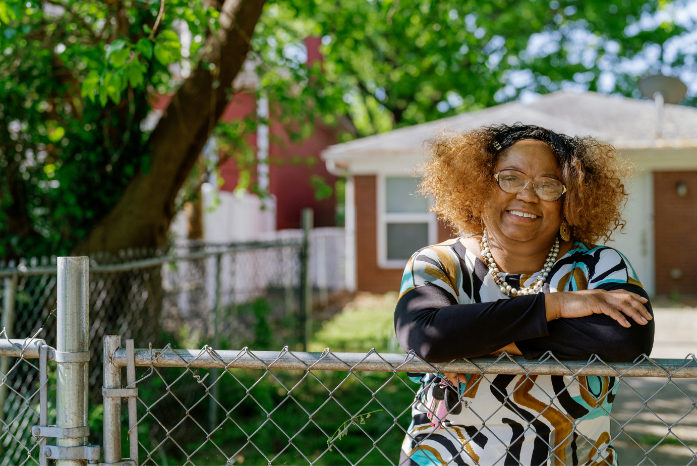 Women leaning on chain linked fence. House in background.