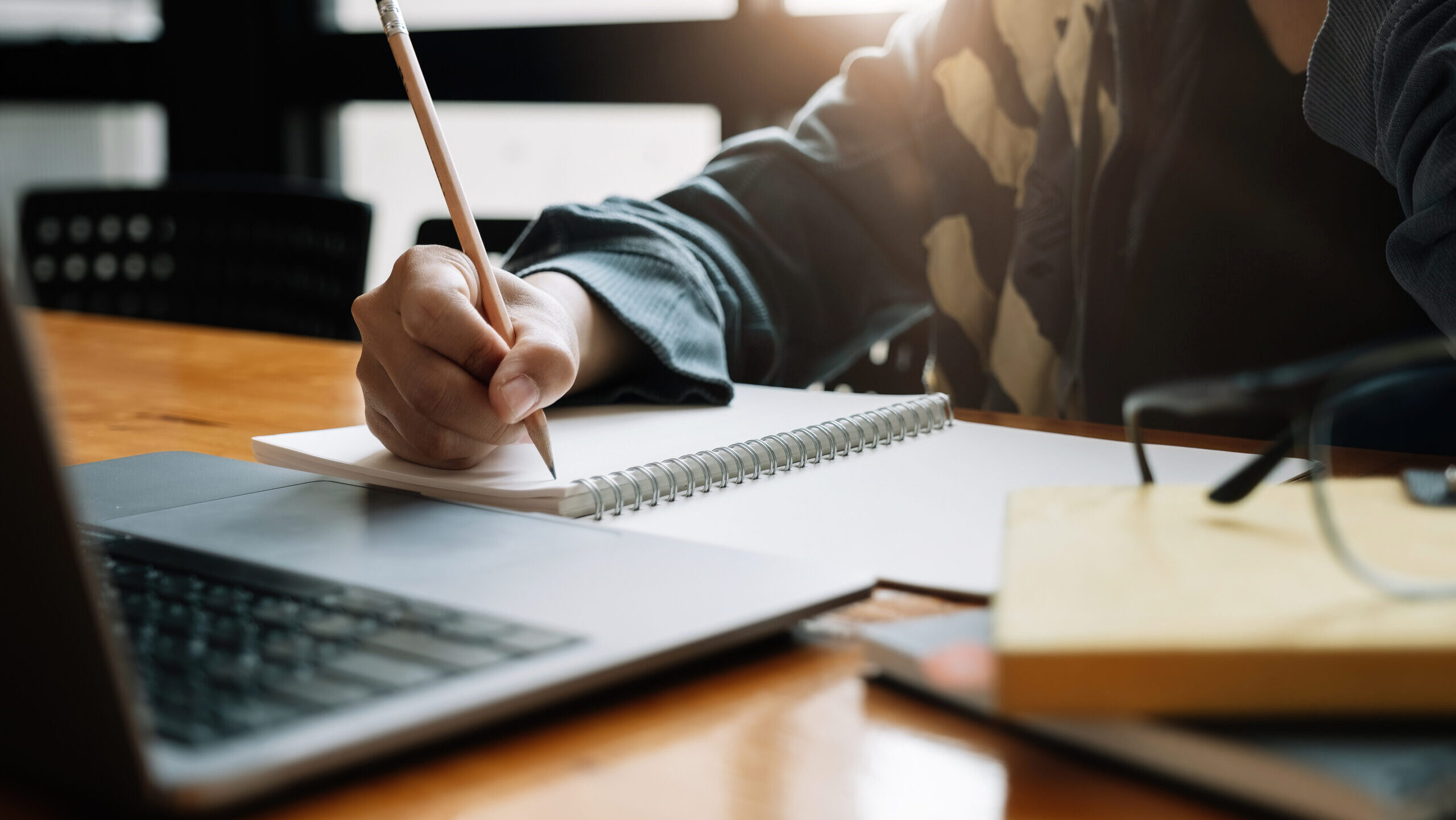 Cropped photo of asian woman writing making list taking notes in notepad working or learning on laptop indoors- educational course or training, seminar, education online concept.