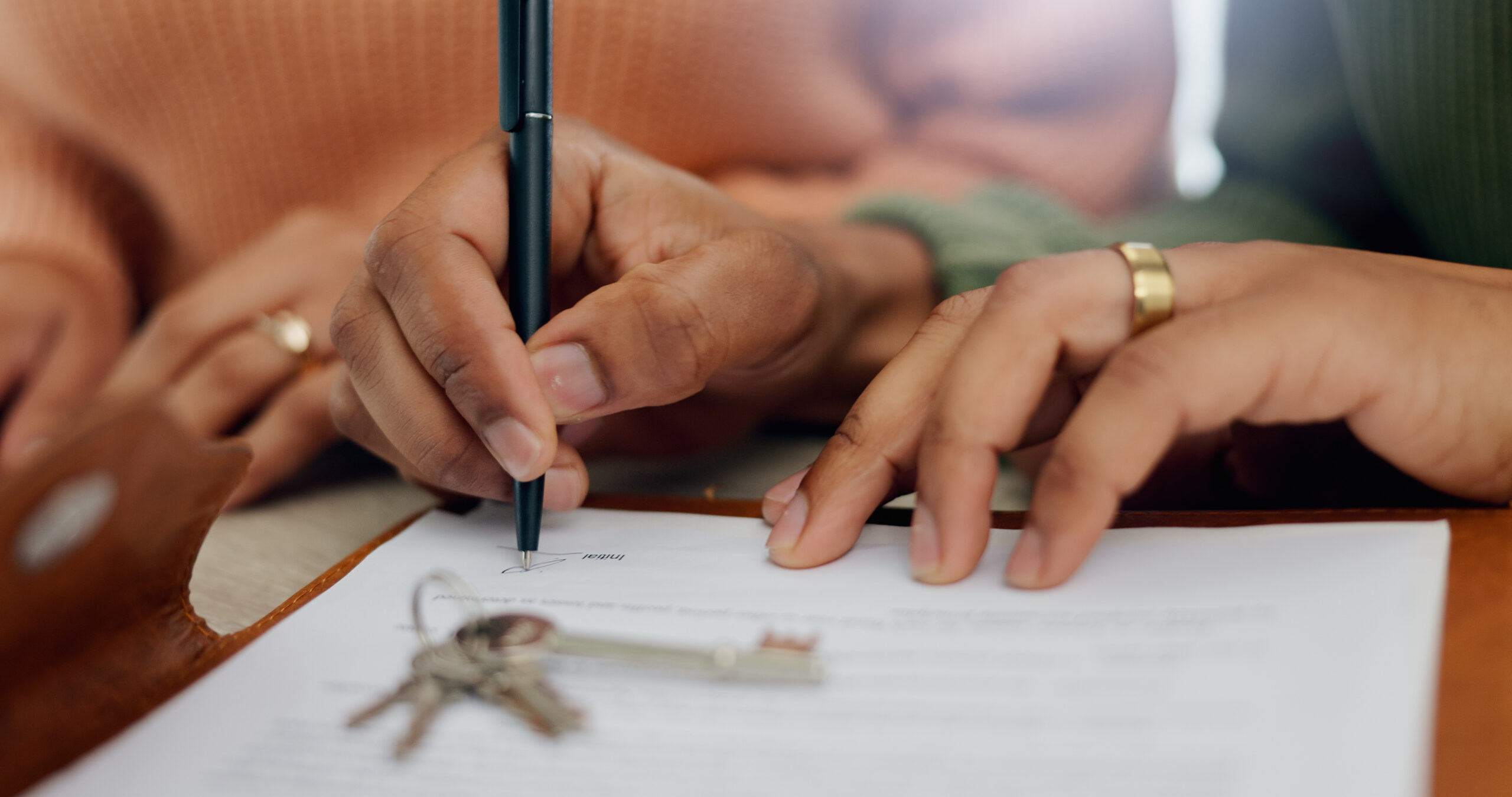 Photo of hands signing a document near house keys